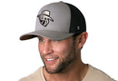 A man with a trimmed beard wears a Haka Hat JBR Silver Logo gray and black metallic leather snapback by Haka Hat, smiling and looking to the side in a light shirt against a white background.
