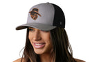 A woman with long brown hair smiles, wearing a Haka Hat JBR Logo Gray Black Poly Leather Snapback by Haka Hat. The hat has a stylized western logo, comfort-fit sweatband, and is perfect for all-day wear. Background is plain white.