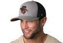A smiling man with a short beard wears the Haka Hat JBR Logo Gray Black Poly Leather Snapback, featuring a stylized cowboy hat and face logo. The comfort-fit sweatband adds to his enjoyment as he poses in a light beige shirt against a white background.