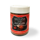 A clear jar with a white lid, labeled SALTOPIA Infused Sea Salts from the Saltopia Spice Lovers Gift Set—featuring a red label with seasoning images and a hand holding a spoon—perfect for adding bold, flavorful sea salt to any dish.