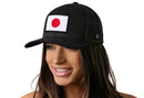A woman smiles, wearing the Haka Hat Japanese Flag Trucker Hat | Black Japan Snapback by Haka Hat, featuring an embroidered Japanese flag patch with a white background and red circle, set against a plain white backdrop.