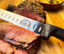 A sleek SpitJack barbecue knife from the Barbecue Knife Bundle, complete with a brisket set, chef's knife, sharpening hone, paring knife, and case, sits gracefully on the cutting board, prepared to handle any culinary challenge.