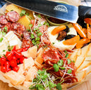 A charcuterie board with assorted meats, cheeses, dried fruits, red peppers, and microgreens is elegantly presented alongside the SpitJack 8 Inch Chef Knife from the SpitJack 8 Inch Chef Knife and 11 Inch Sharpening Hone Combo—a sophisticated addition to any kitchen knife set.