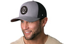 A smiling man with a trimmed beard wears the Haka Hat Kansas City Trucker Hat | Gray-Black KC X Snapback and a light beige shirt, posed against a white background.