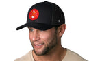 A smiling man with a short beard wears the Haka Hat Kansas City Trucker Hat | Red Gold KC X | Black Snapback by Haka Hat and a beige shirt, against a white background.