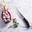A halved dragon fruit with white flesh and black seeds rests on marble beside fresh sage leaves and the Messermeister Kawashima Utility Knife - 6", featuring a dark wooden handle, ideal for kitchen prep.