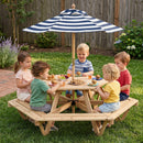 Five kids enjoy snacks and treats at the Kids Hexagonal Picnic Table with Umbrella and 6 Benches by DirectDeals, seated together under the blue and white striped umbrella in a grassy backyard.