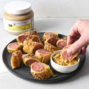 A hand dips a seasoned sausage roll into barbecue mustard on a black plate. In the background are more sliced sausage rolls and a quart jar of Terrapin Ridge Farms Smokey Onion Mustard, the perfect burger condiment.