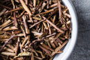 A close-up of a white bowl filled with World Spice Toasted Kukicha by World Spice, a traditional Japanese twig tea made from organic toasted stems and twigs, celebrated for its low caffeine content, displayed on a gray surface.