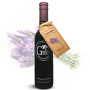 A dark glass bottle of Georgetown Olive Oil Co. Lavender Balsamic Vinegar from Georgetown Olive Oil Co., made with aged balsamic vinegar from Modena, Italy, displays a tag decorated with delicate lavender flowers and is set against a softly blurred background featuring a bouquet of lavender.