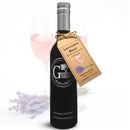 A bottle of Georgetown Olive Oil Co. LAVENDER ROSÉ White Balsamic Vinegar, complete with a tag, is displayed in front of a glass filled with pink liquid and a sprig of lavender. Crafted from barrel aged Modena white balsamic in Italy, this refined vinegar delights with delicate floral notes and a crisp, refreshing finish.