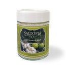 A glass jar of Saltopia Lime Garlic Salt from SALTOPIA Infused Sea Salts features a green label with garlic cloves and limes, plus a white plastic lid. The jar is shown against a white background.