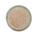 A glass jar of SALTOPIA Infused Sea Salts' Lime Garlic Salt, filled with coarse, light pink crystals and shown from above on a white background—perfect as a finishing salt.