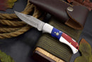 The Handcrafted Damascus Steel Pocket Knife by Texan Knives features a Texas flag handle and comes with a leather sheath, shown resting on rope among autumn leaves and rustic wood—perfect as a collectible EDC gift.