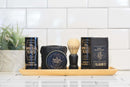 A wooden tray displays men’s grooming essentials—including The Immaculate Beard’s Immaculate Natural Beard Balm For Men With Lightweight Hold, a shaving brush, and a potted plant—against a white tiled background. The arrangement emphasizes the role of natural beard balm in maintaining a refined daily routine.