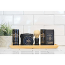 A wooden tray holds beard care essentials from The Immaculate Beard, featuring the Immaculate Fast Absorbing Beard Oil For Men Softens Skin, along with balm, beard wash, and a shaving brush—ideal for daily beard conditioning. A green plant is placed in the background against a white tiled wall.
