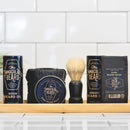 A wooden tray displays beard care products—including beard oil, beard balm, beard wash, and a shaving brush—alongside The Immaculate Beard’s Dark Shave Soap Puck, crafted with kaolin clay for sensitive skin, all set on a counter with a white tiled background.