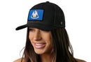 A woman with long brown hair smiles while wearing the Haka Hat Louisiana Flag Trucker Hat, a black snapback featuring the state flag emblem. The background is plain white.