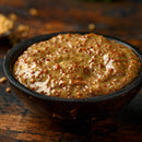 A small black bowl holds SALTOPIA Smoky Sweet Mustard Seasoning Low Sodium: MACK'S BACK, showing its thick, seeded texture on a rustic wooden surface—perfect as a flavorful, low sodium seasoning for healthy cooking.