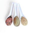 Three white ceramic spoons filled with SALTOPIA Infused Sea Salts in beige, pink, and brown sit side by side—showcasing the Saltopia Mediterranean Kitchen Gift Set, perfect for any culinary enthusiast.