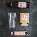 A Budweiser beer bottle, a Swanky Badger Pint Glasses - Set of 4: The Heirloom, a tan can cooler with a circular logo, and a wooden bottle opener arranged on a dark surface.