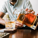 A person pours whiskey from a glass decanter into a matching tumbler, both Heirloom Whiskey Glasses personalized with the name Lawson.