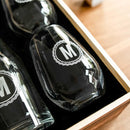 Two clear glass Wine Decanter - The Medalist decanters engraved with a circular emblem featuring the letter M, nestled in a wooden box as a custom wine gift.