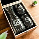 A glass wine decanter and two stemless wine glasses, each featuring an M monogram, inside a wooden display box as part of The Heirloom wine decanter set by Swanky Badger.