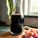 A Swanky Badger Wine Decanter - The Diamond filled with red wine, etched with the name SMITH inside a diamond shape, sitting on a wooden board next to a bunch of grapes.