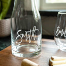 Clear glass Wine Decanter - The Script engraved with the name Smith in a script design, sitting on a wooden board next to a matching wine glass.