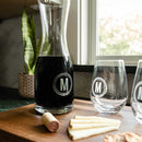 A Wine Decanter - The Medalist set including two engraved wine glasses with the letter M, arranged on a wooden board with cheese and a cork.