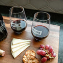 Two personalized stemless wine glasses from the Wine Decanter - The Classic collection, engraved with the names Rachel and Wyatt, filled with red wine on a wooden board with cheese, crackers, and red grapes.