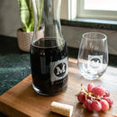 Swanky Badger Wine Decanter - The Heirloom set, featuring a glass decanter and matching stemless glass etched with the letter M, resting on a wooden board next to a bunch of grapes and a cork.