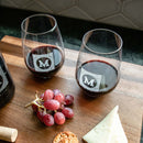 Two personalized Wine Decanter - The Heirloom wine glasses engraved with a square emblem containing the letter M sit on a wooden board next to a cluster of red grapes, a cracker, and a slice of cheese.