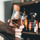 A hand holds an amber-filled Whiskey Glasses: Heirloom, custom engraved with the name ALLEN and an ornate border.