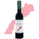 A bottle of Georgetown Olive Oil Co. Picholine (MOROCCO) Extra Virgin Olive Oil sits in front of a pink silhouette map of Morocco, featuring a red highlighted region that matches the shape displayed on the bottle’s label. This cold-pressed olive oil from Georgetown Olive Oil Co. offers high polyphenol content, delivering robust flavor and exceptional quality.