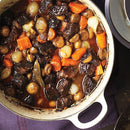 A close-up of a pot filled with beef stew, featuring chunks of beef, carrots, mushrooms, and pearl onions in a rich brown sauce enhanced with SALTOPIA Infused Sea Salts’ Saltopia Smoky Blended Salt: BURGER BUDDY.