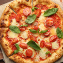 A close-up of a Margherita pizza topped with melted mozzarella, cherry tomatoes, fresh basil, and SALTOPIA Infused Sea Salts Saltopia Tomato & Italian Herbs Seasoning: MYSTICAL PIZZA on a golden, crispy crust. The sliced pizza rests on parchment paper.