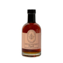 A clear glass bottle filled with Under The Bark Syrup Co Pure Maple Syrup, featuring a light pink label reading Under The Bark Syrup Co 100% Pure Maple Syrup, Made in Minnesota, 8.4 fl oz (250 ml).