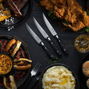 A table set on dark wood features fried chicken, burgers, ribs, sides, whiskey, cornbread, and a Messermeister Avanta Damascus Block Set – 10 Piece knife by Messermeister.