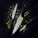 The Messermeister Blacksmith Chef's Knife - 8", featuring a black handle and crafted from German stainless steel, is displayed on a dark surface with herbs, salt, and mushrooms in a neat flat lay. Brand: Messermeister.