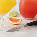 The Messermeister Blacksmith Paring Knife - 3.5" rests on a white surface next to sliced blood orange, lime slices, a bright yellow drink in a stemmed glass, and a red drink in the background.
