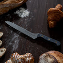 The Messermeister Custom Next Level 5-Piece Magnetic Knife Block Set from Messermeister is artfully arranged on a dark wooden table amidst an assortment of breads, croissants, and scattered flour—showcasing both sophisticated design and the efficiency that defines an organized kitchen storage solution.