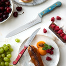 Two knives from the Messermeister Custom Red 4 Piece Steak Knife Set are displayed among assorted fruits, an éclair, and chocolate cake with raspberries on a white surface.