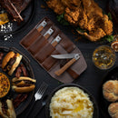 A top-down view of fried chicken, sliders, mashed potatoes, biscuits, a drink, and the Messermeister Folding Steak Knife Set in Leather Roll (4 Piece), all on dark plates atop a dark surface.