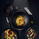 A black wok of vibrant stir-fried vegetables rests on a dark table, surrounded by stuffed mushrooms, sliced vegetables cut with the Messermeister Kawashima Paring Knife - 3.5", a knife, chopsticks, ginger, and herbs.