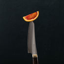 A slice of blood orange balances on the tip of a sharp Messermeister Kawashima Magnet Block Set - 5 Piece knife, set against a plain dark background.