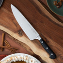 A Messermeister Meridian Elite Starter Set - 3 Piece with black handles sits on a wooden cutting board, alongside cinnamon sticks, a plate of pecans, and a pie slice topped with whipped cream.