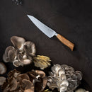 A Messermeister Oliva Elite O.T. Prep Knife - 6.5" with a wooden handle rests on a dark surface, surrounded by clusters of various oyster mushrooms.