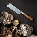 The Messermeister Oliva Elite Nakiri Knife - 6.5" features a German-forged blade and olive wood handle, shown on a dark surface among beige, gray, and white oyster mushrooms—ideal for precise vegetable preparation.